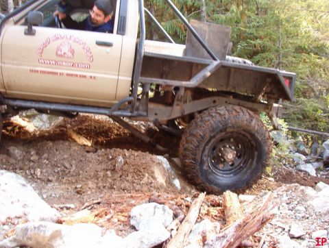 Tan pickup truck with custom flatbed off-roading on a rocky trail.