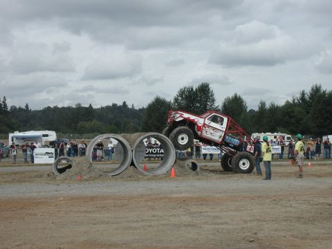 Monster truck with flames and red roll cage driving over concrete pipes.