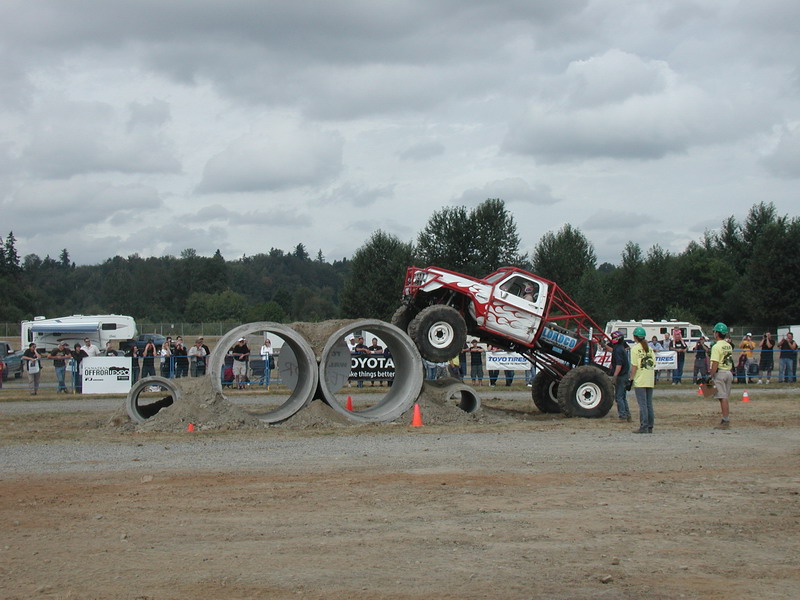 Monster truck with flames and red roll cage driving over concrete pipes.
