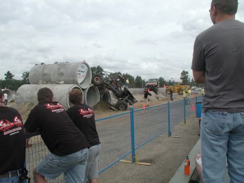 Off-road buggy climbing over concrete pipes with spectators watching.