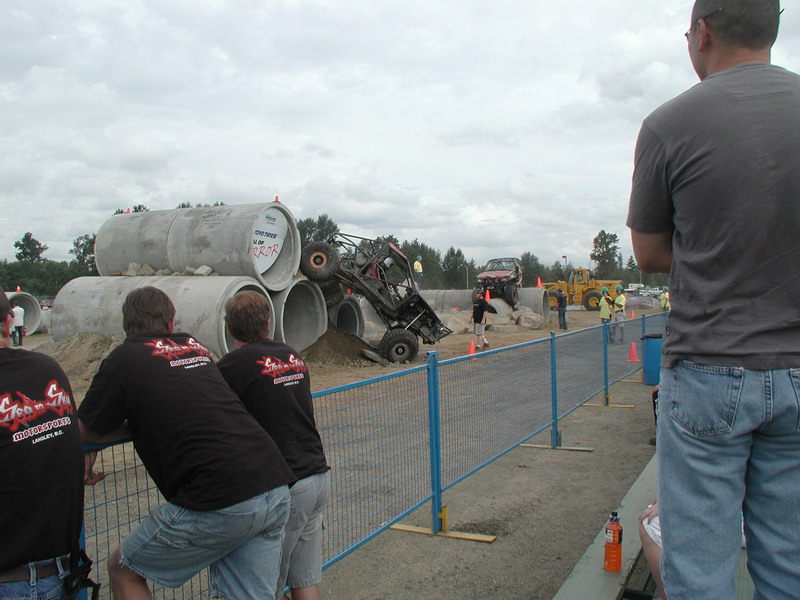 Off-road buggy climbing over concrete pipes with spectators watching.