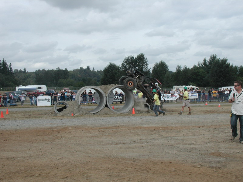 Off-road buggy airborne over concrete pipes with spectators in the background