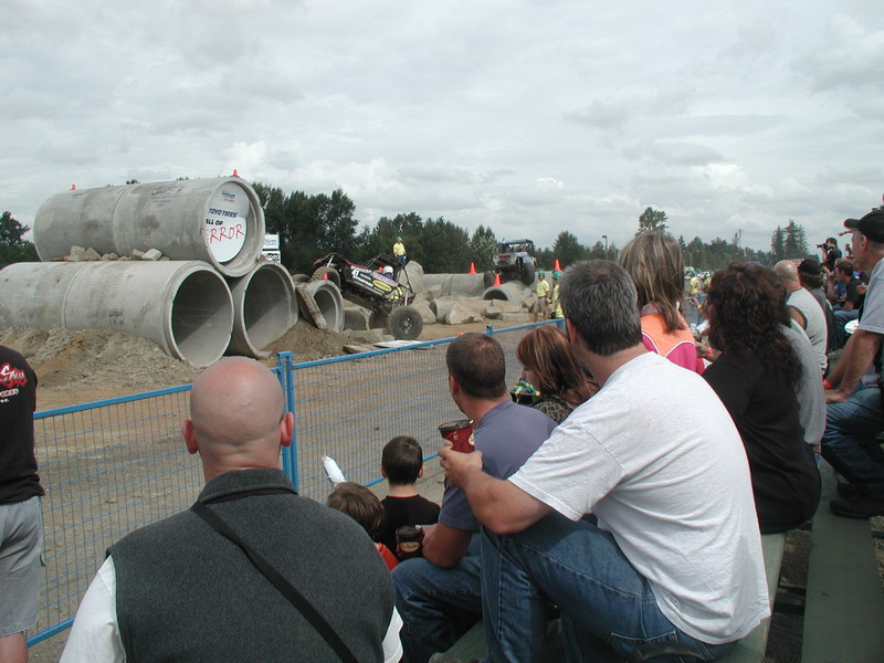 Off-road buggy driving through concrete pipes obstacle course with spectators.
