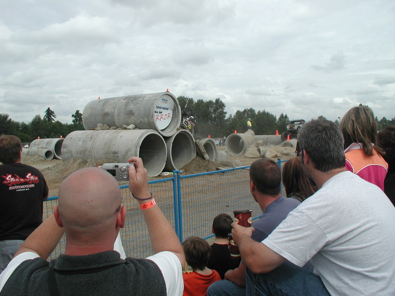 Motocross rider on a dirt bike jumping over concrete pipes, spectators watching.