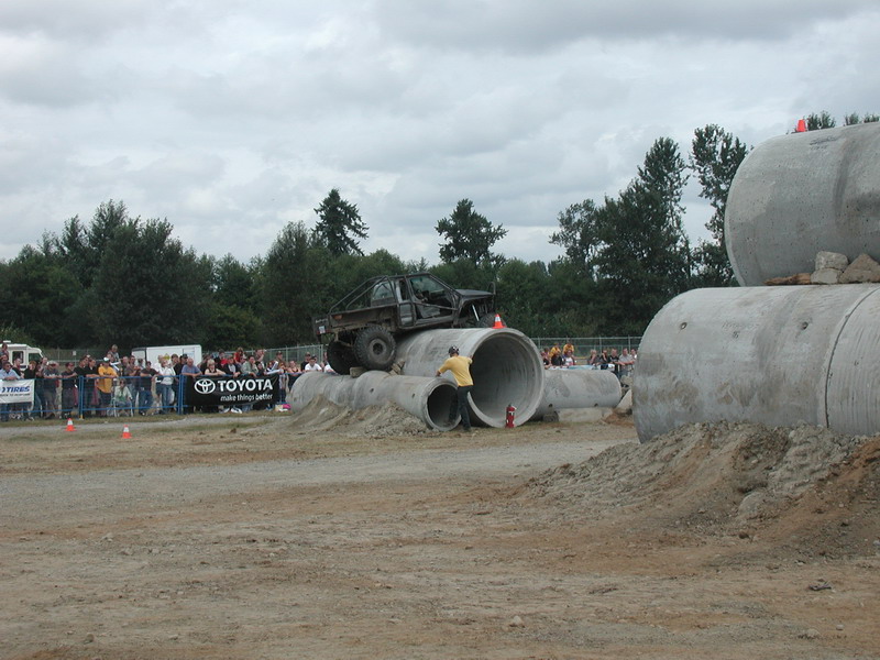 Modified pickup truck driving over concrete pipes with spectators watching.