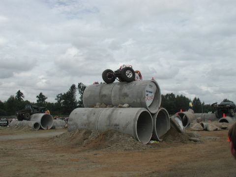 Off-road vehicles on a course with concrete pipes and dirt mounds.