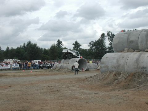 White Toyota pickup truck driving over concrete pipes with spectators watching.