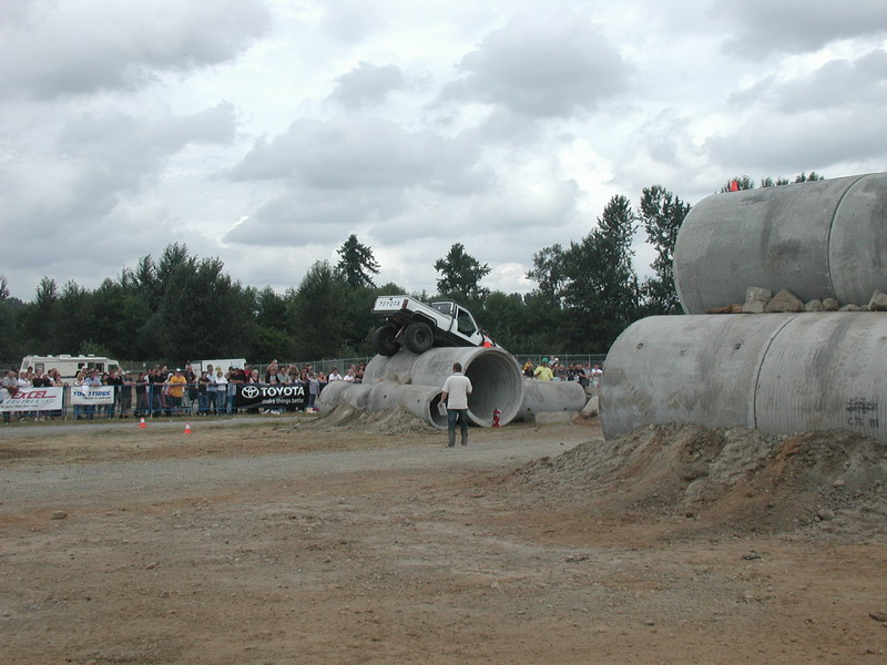White Toyota pickup truck driving over concrete pipes with spectators watching.