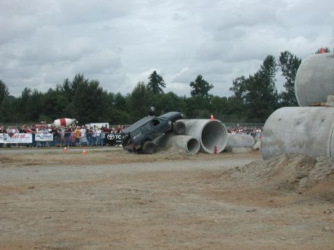 Dark blue Jeep Cherokee climbing over concrete pipes during an off-road event.
