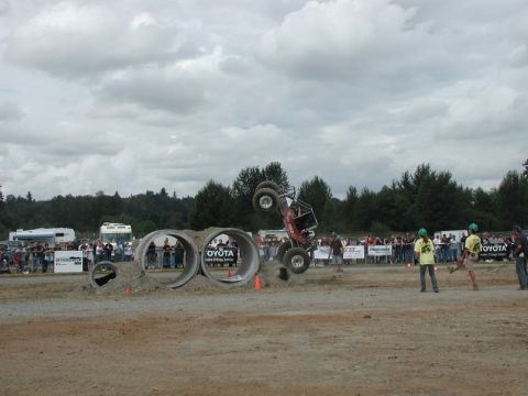 Off-road buggy flipping over concrete pipes with spectators watching.
