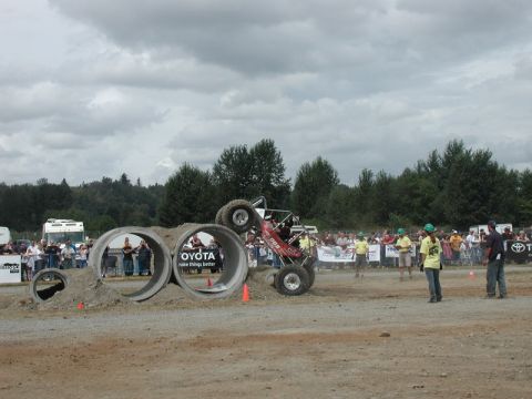 Off-road buggy driving through concrete pipes at an event with spectators.