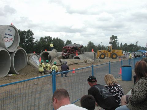 Red off-road buggy on a concrete pipe obstacle course with a yellow loader in the background.