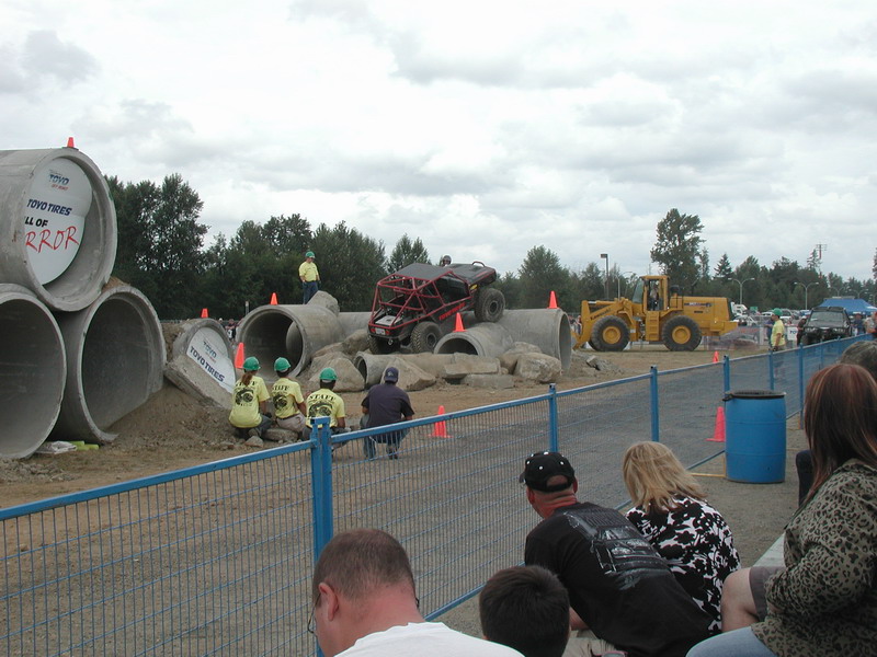 Red off-road buggy on a concrete pipe obstacle course with a yellow loader in the background.