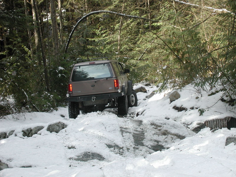 Tan Ford Explorer driving on a snowy trail in a forest.