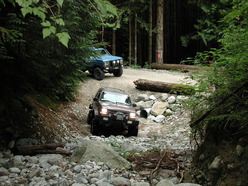 Two off-road vehicles on a rocky forest trail.