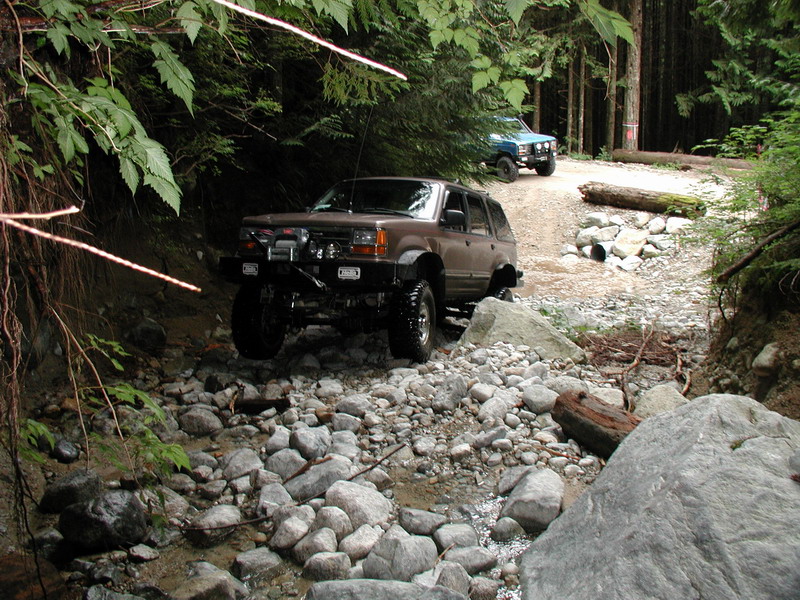 Brown and blue SUVs on a rocky, wooded off-road trail.