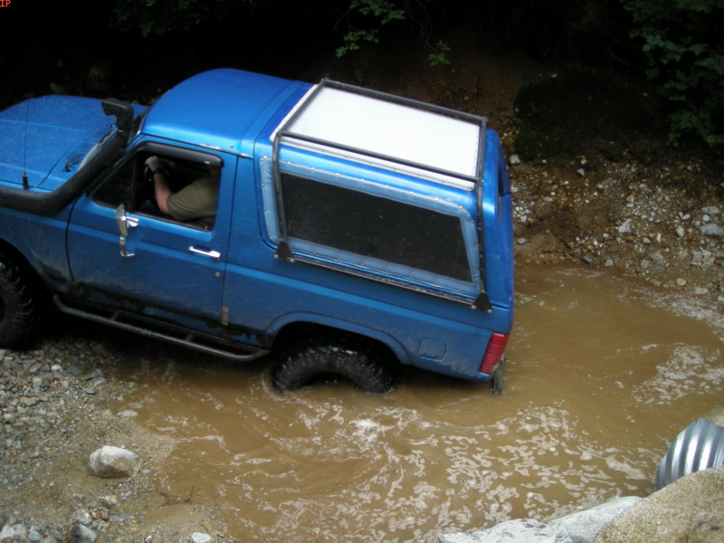 Blue Ford Bronco with snorkel driving through a muddy stream.