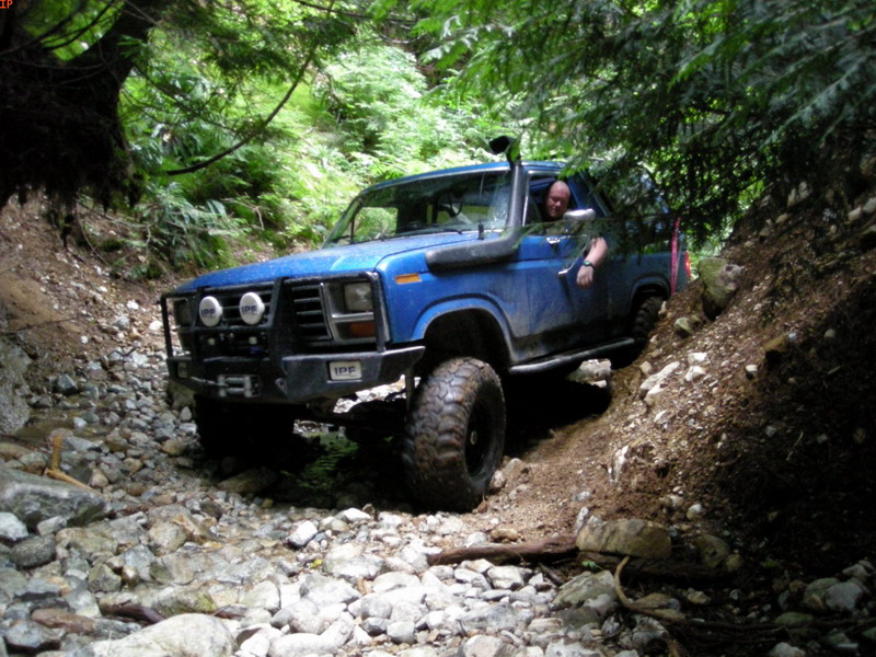 Blue Ford Bronco off-roading on a rocky trail with a snorkel and custom bumper.