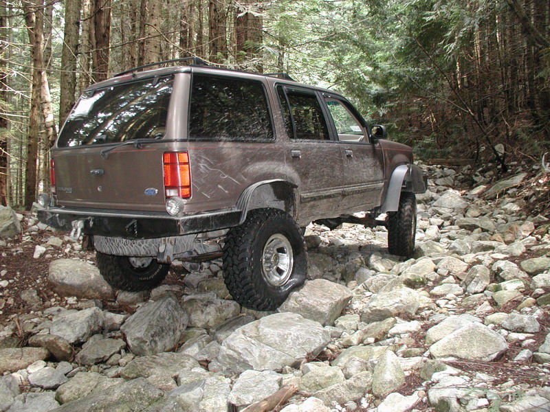 Brown lifted SUV on a rocky trail in a forest.