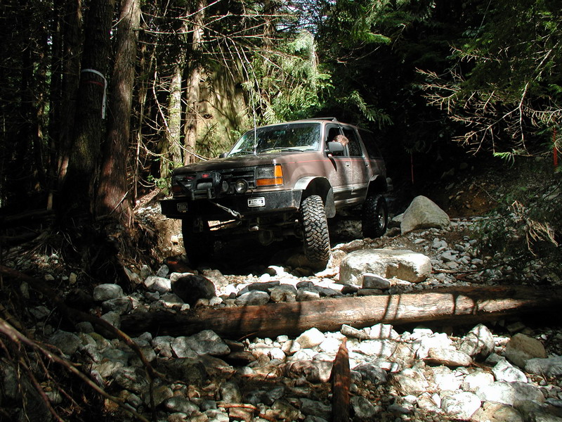 Brown Ford Explorer off-roading on a rocky, wooded trail.