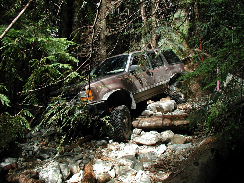 Brown SUV with off-road tires on a rocky, wooded trail.