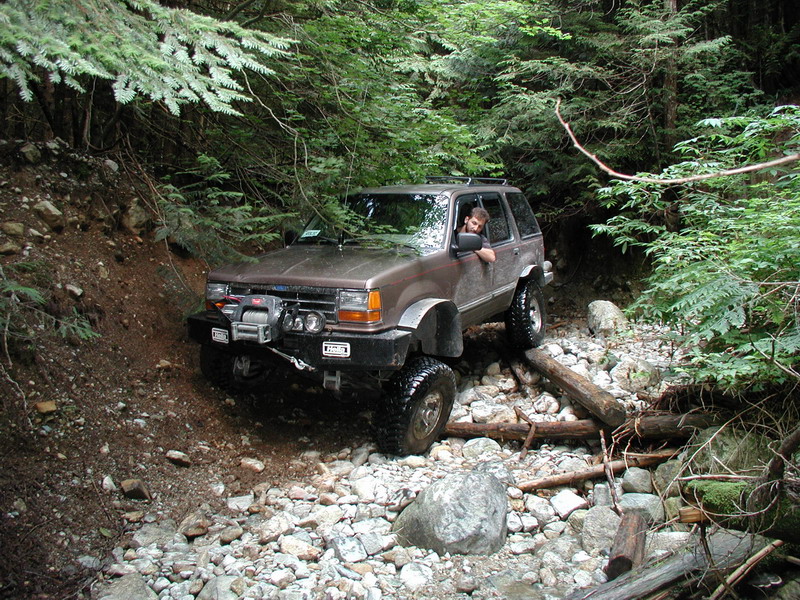 Brown SUV with winch and off-road tires on a rocky forest trail.