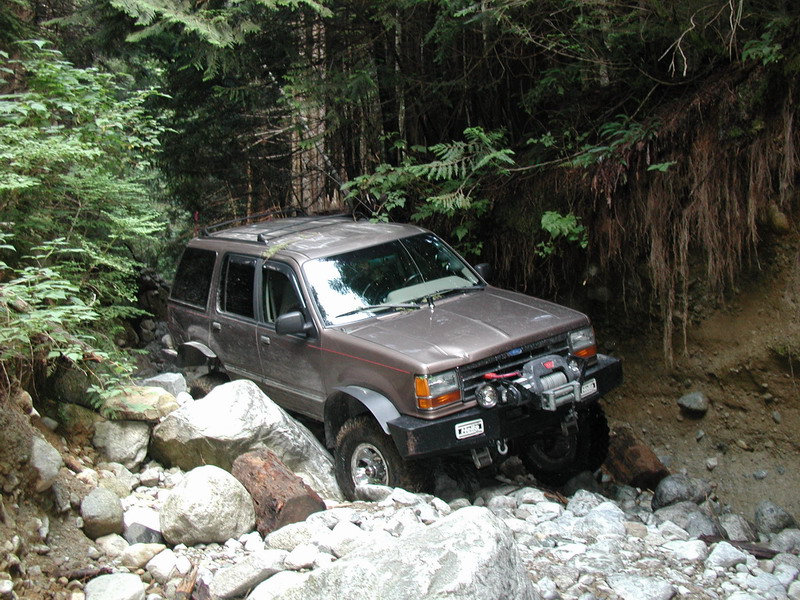 Brown SUV with winch on front bumper driving on a rocky, wooded trail.
