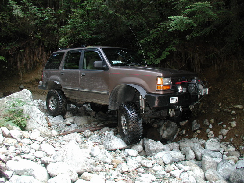 Lifted brown SUV on a rocky trail with trees in the background.