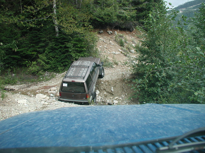 Brown SUV on a steep, rocky off-road trail, viewed from behind another vehicle.