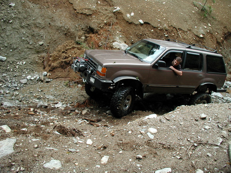 Brown SUV with off-road tires driving through a rocky, muddy ravine.