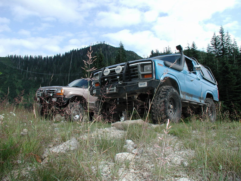 Two off-road SUVs parked on a hillside, one blue Ford Bronco with snorkel.