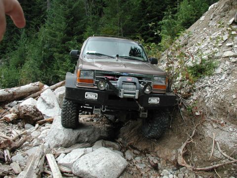 1985 Ford Bronco - A brown Ford Explorer is navigating a rocky, wooded trail, with its front tires on large boulders and a winch mounted on the aftermarket bu…
