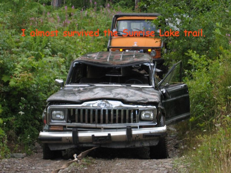 Damaged Jeep SUV with an orange truck behind it on a trail.