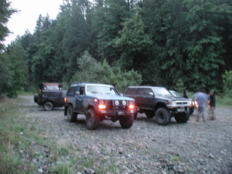 Three off-road SUVs parked on a gravel road in a forest.