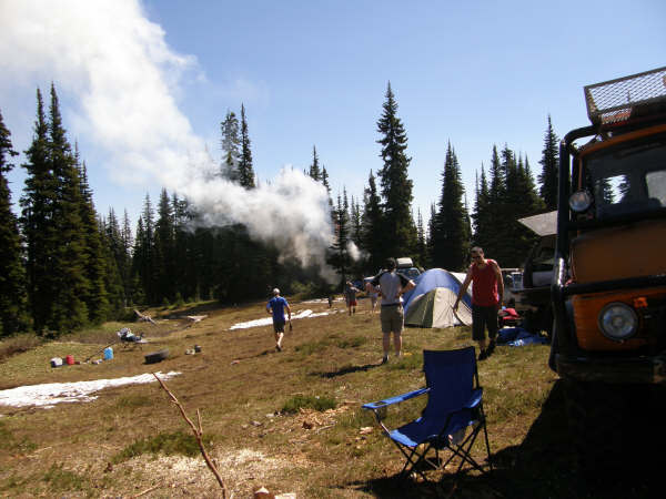 Orange off-road vehicle parked at a campsite with people and tents.