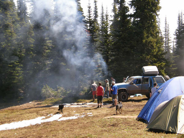 Blue SUV parked at a campsite with tents and people in a wooded area.