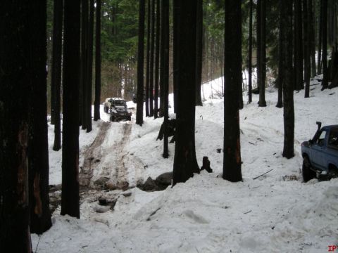 1985 Ford Bronco - A blue Ford Bronco is parked on a snowy forest road next to a track made by off-road vehicles. Another off-road vehicle is visible further…