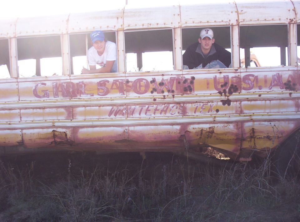 Rusty school bus with two people in windows, text reads "GIRL SATOWN TUSCA" and "WHITEFACE TEX."