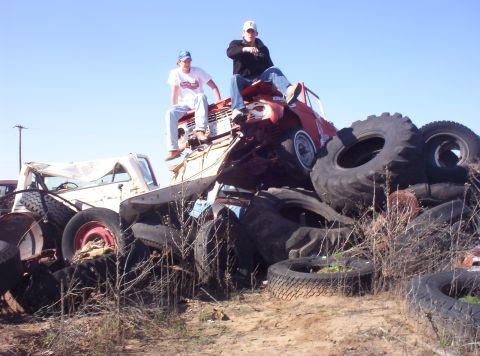 1988 Ford Bronco - Two individuals perched atop a heap of discarded vehicles and tires under a clear blue sky.