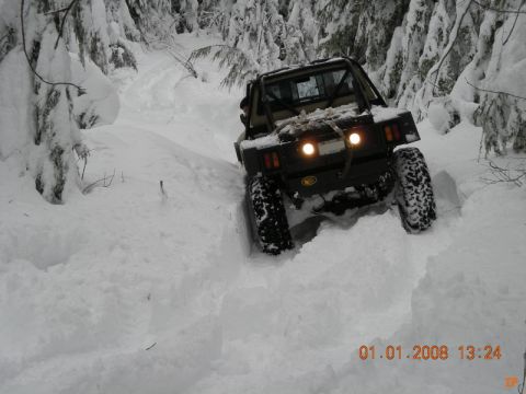 1985 Ford Bronco - The rear view of a dark-colored off-road vehicle, likely a modified SUV or truck, navigates a deep snow-covered trail surrounded by snow-la…