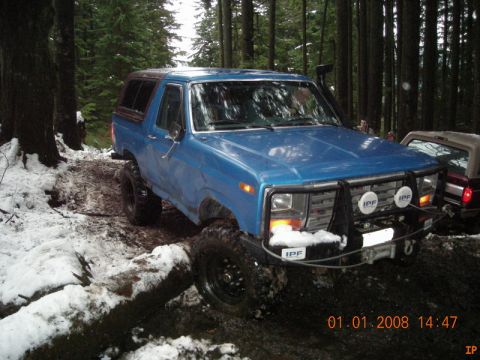 1985 Ford Bronco - A blue 1980s Ford Bronco is parked on a muddy, snow-dusted forest trail. The vehicle has a bull bar with IPF lights and a winch mounted on…