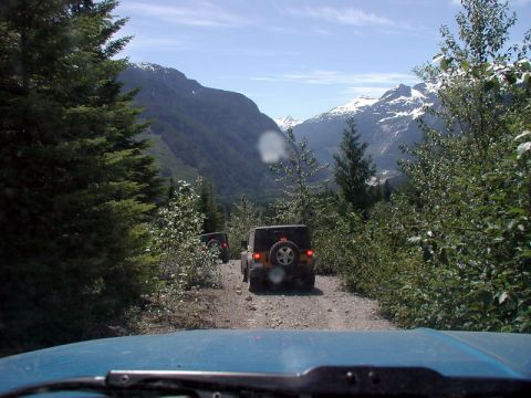 1985 Ford Bronco - The view from inside a blue vehicle looking out at a dirt road with two Jeep Wranglers ahead. Snow-capped mountains are visible in the dist…