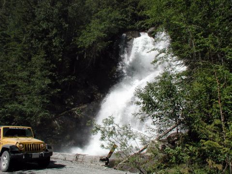 Yellow Jeep Wrangler parked by a waterfall in a forest.