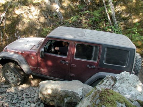 Maroon Jeep Wrangler Rubicon off-roading over rocks and boulders.