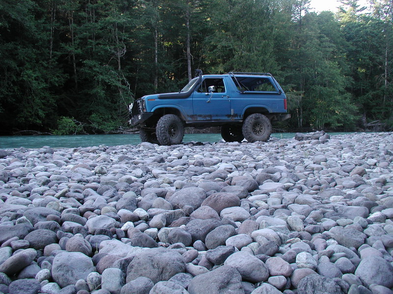 Blue Ford Bronco parked on a rocky riverbed next to a turquoise river.