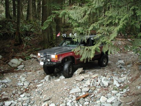 Lifted red and gray Ford Explorer on a rocky forest trail.