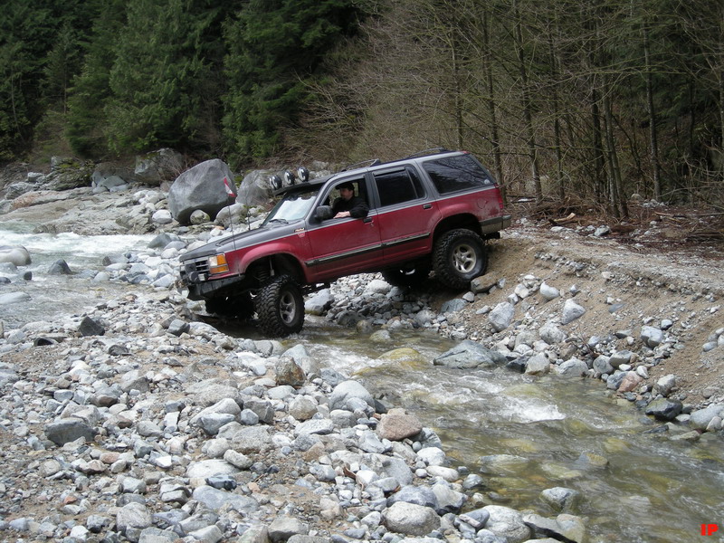 Red and gray SUV off-roading through a rocky riverbed.