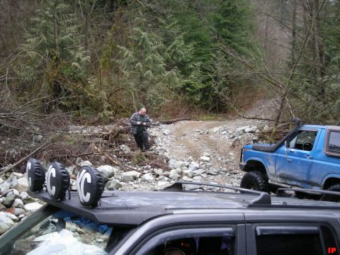Blue Ford Bronco with snorkel on a rocky trail, man standing nearby.