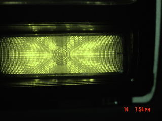 1985 Ford Bronco - Close-up of a vehicle's yellow headlight, showing intricate lens detailing and a website logo.