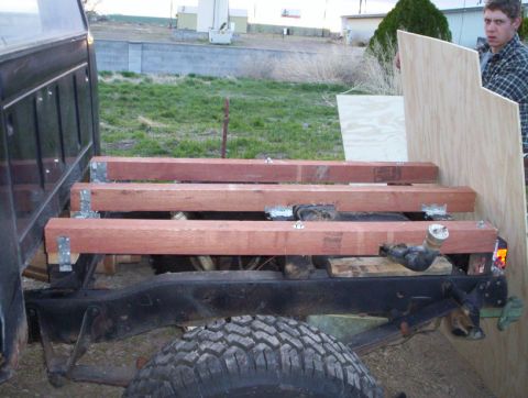 1978 Ford Bronco - A person is holding a piece of plywood near the bed of a truck that has wooden beams secured to it.